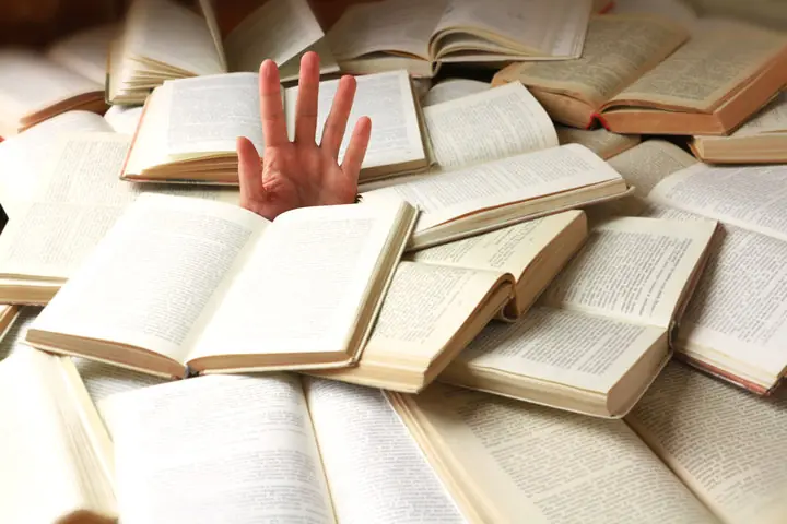 a hand barely sticking out from a sea of open books, drowning in text